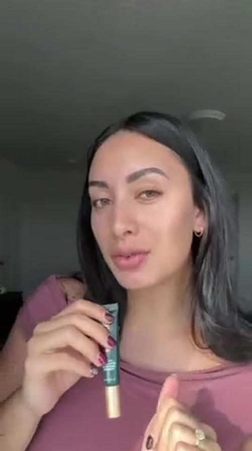 UGC handheld demo of a woman showcasing skincare products. Indoor setting with neutral background, focusing on her face and hands.